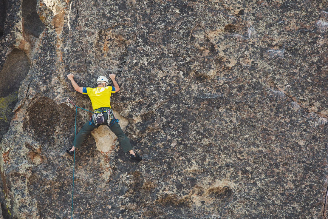 Climber in a helmet scaling a rough rock face in daylight