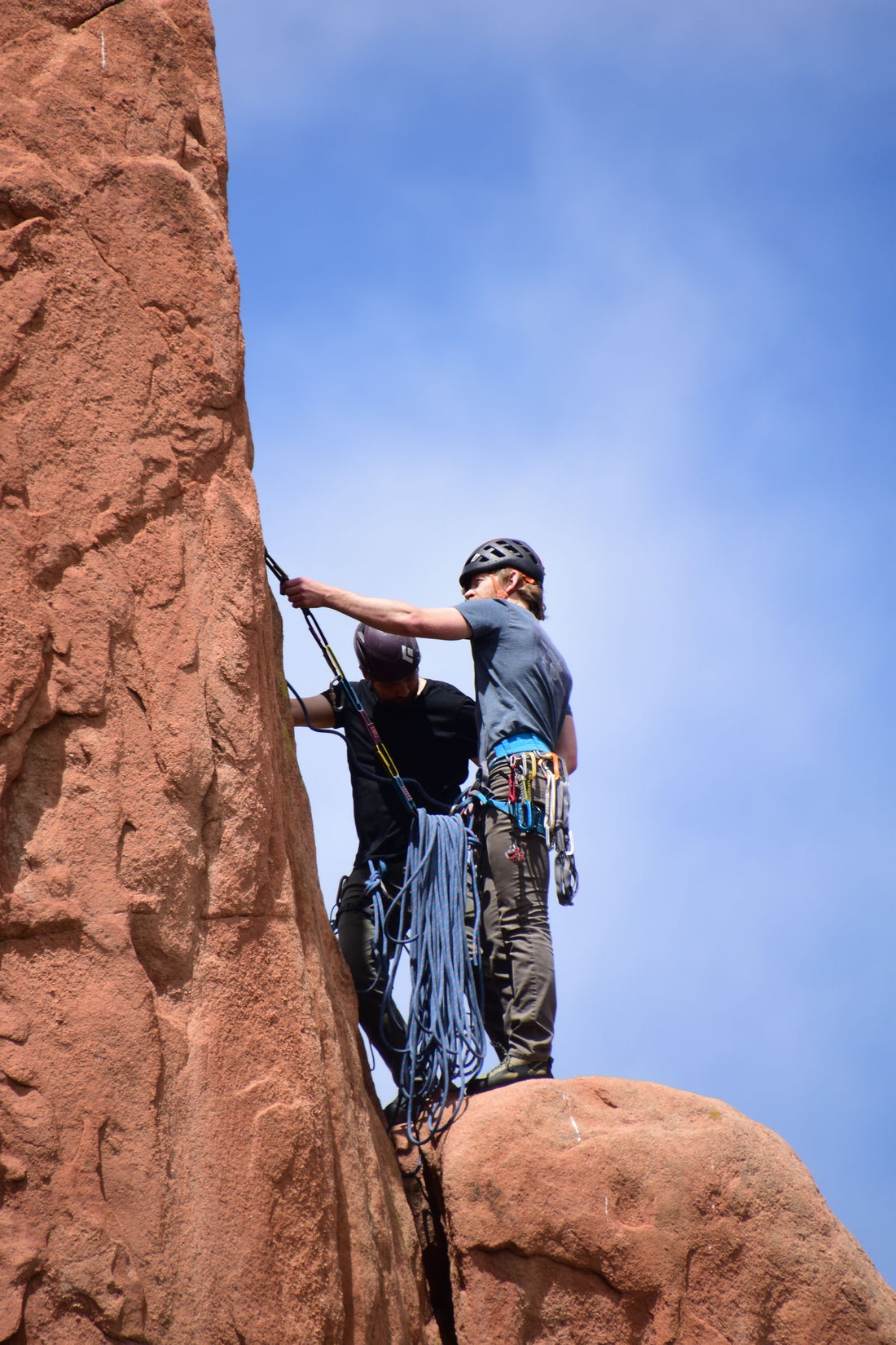 Two climbers in helmets working their way up a red sandstone cliff