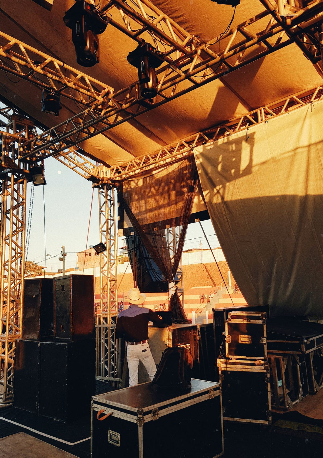 A crew member setting up equipment on a stage at sunset
