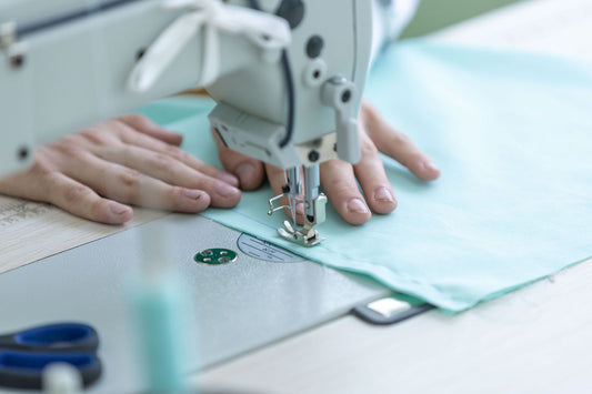 Hands guiding fabric through a sewing machine on a maker's workbench