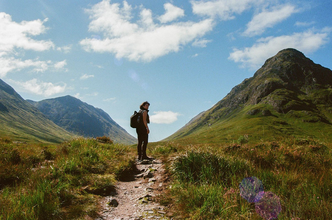 A walker on a path in the Scottish Highlands with mountains behind