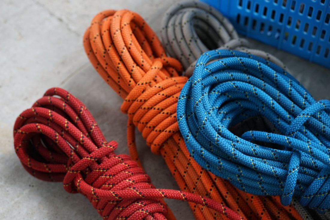 Red, orange and blue climbing ropes coiled up on a concrete floor, each a different colour