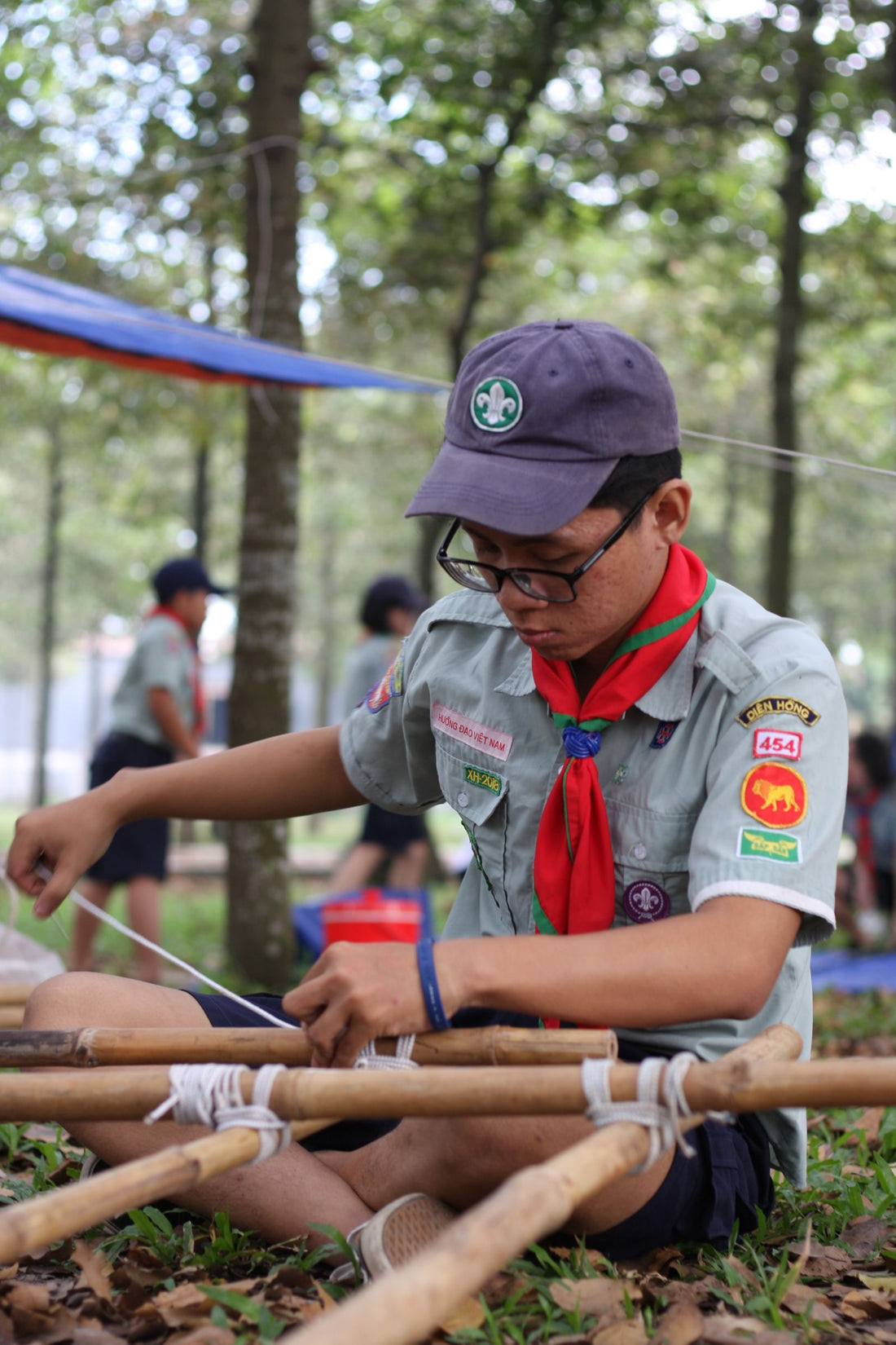A young scout in uniform practising knot tying outdoors at camp