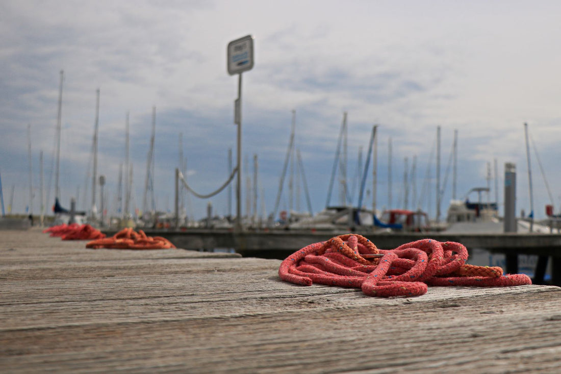 Red mooring ropes coiled on a wooden dock with fishing boats and a grey cloudy sky behind