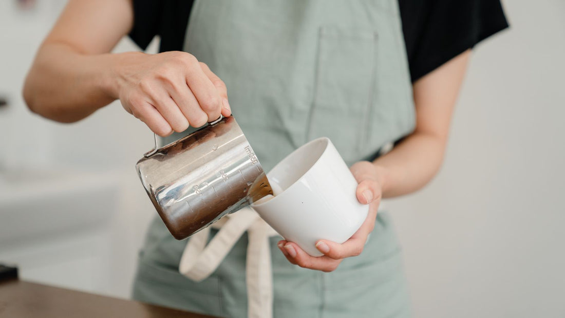 A cafe worker pouring milk from a jug into a cup
