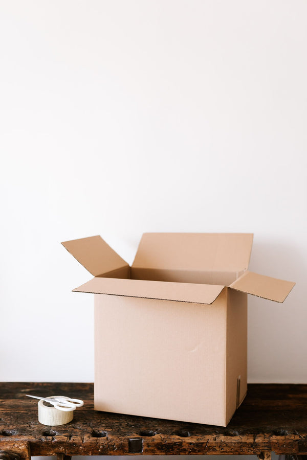 An open cardboard box on a weathered wooden bench with a roll of packing tape and scissors beside it