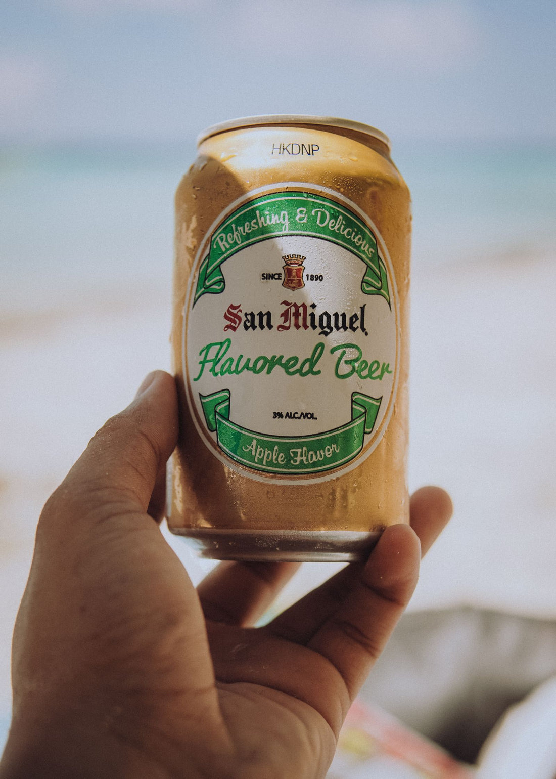 A hand holding a cold can of drink outdoors on a relaxed summer day