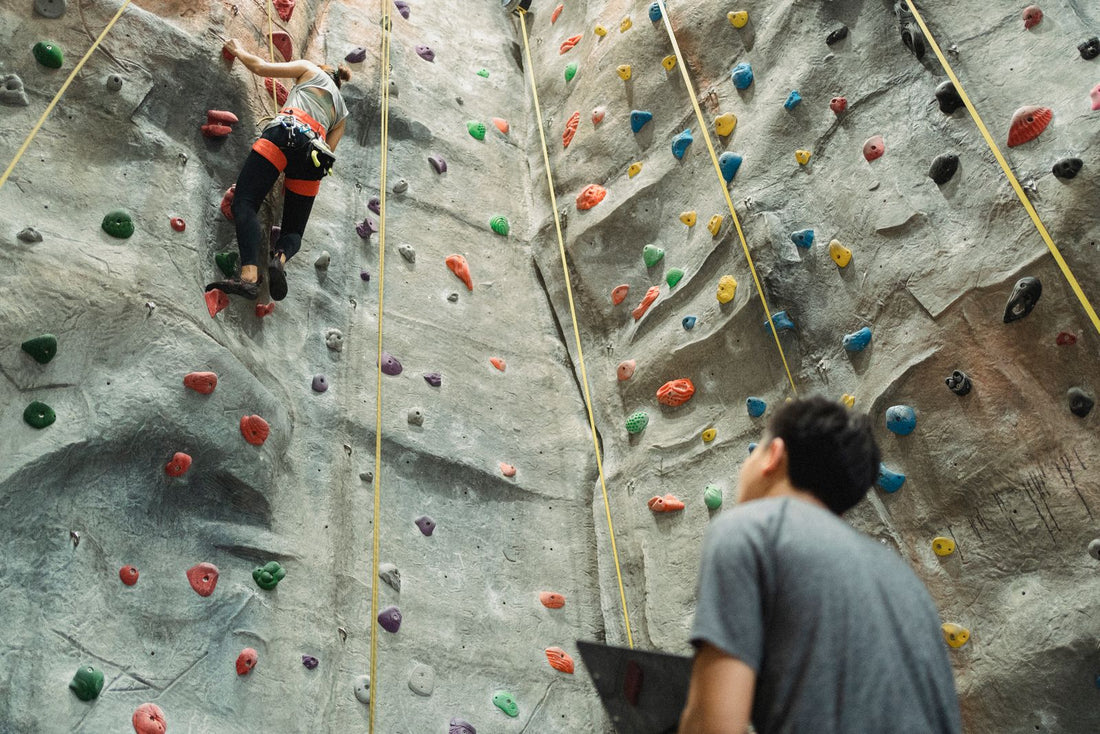 A climber on an indoor climbing wall with their belay partner holding the rope below