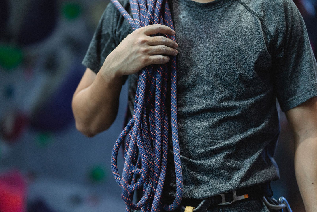 A climber in sportswear holding a dynamic climbing rope beside an indoor climbing wall