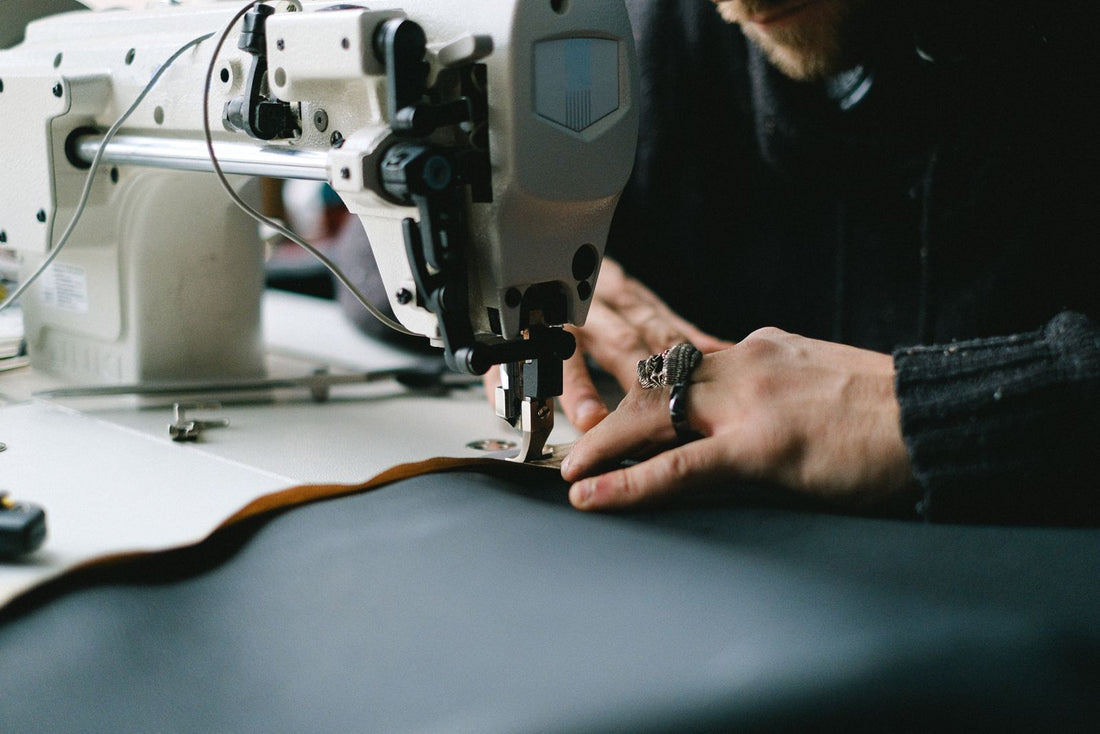 Close-up of a maker's hands guiding fabric through a sewing machine in a workshop