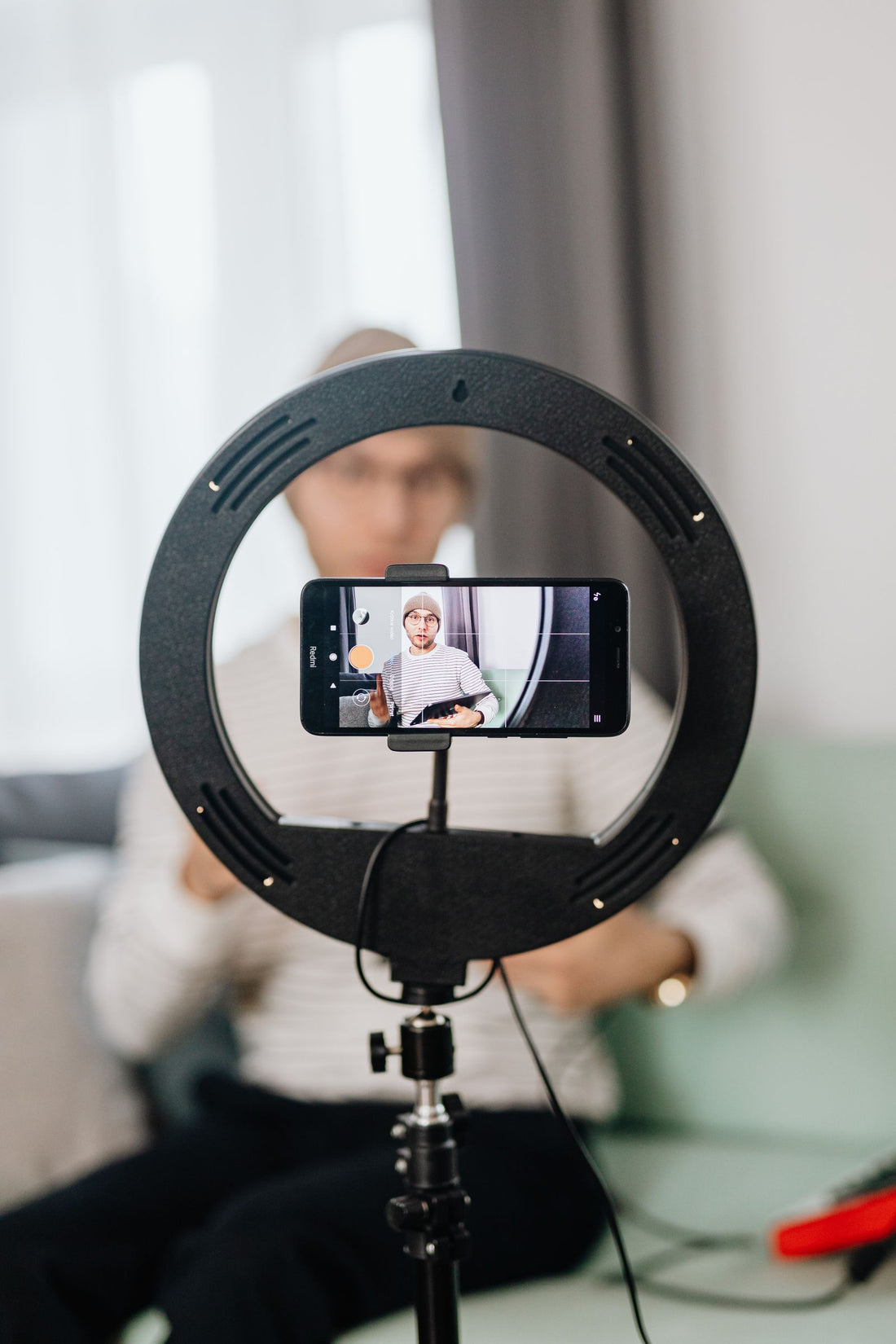 A maker filming himself on a smartphone mounted to a ring light tripod indoors