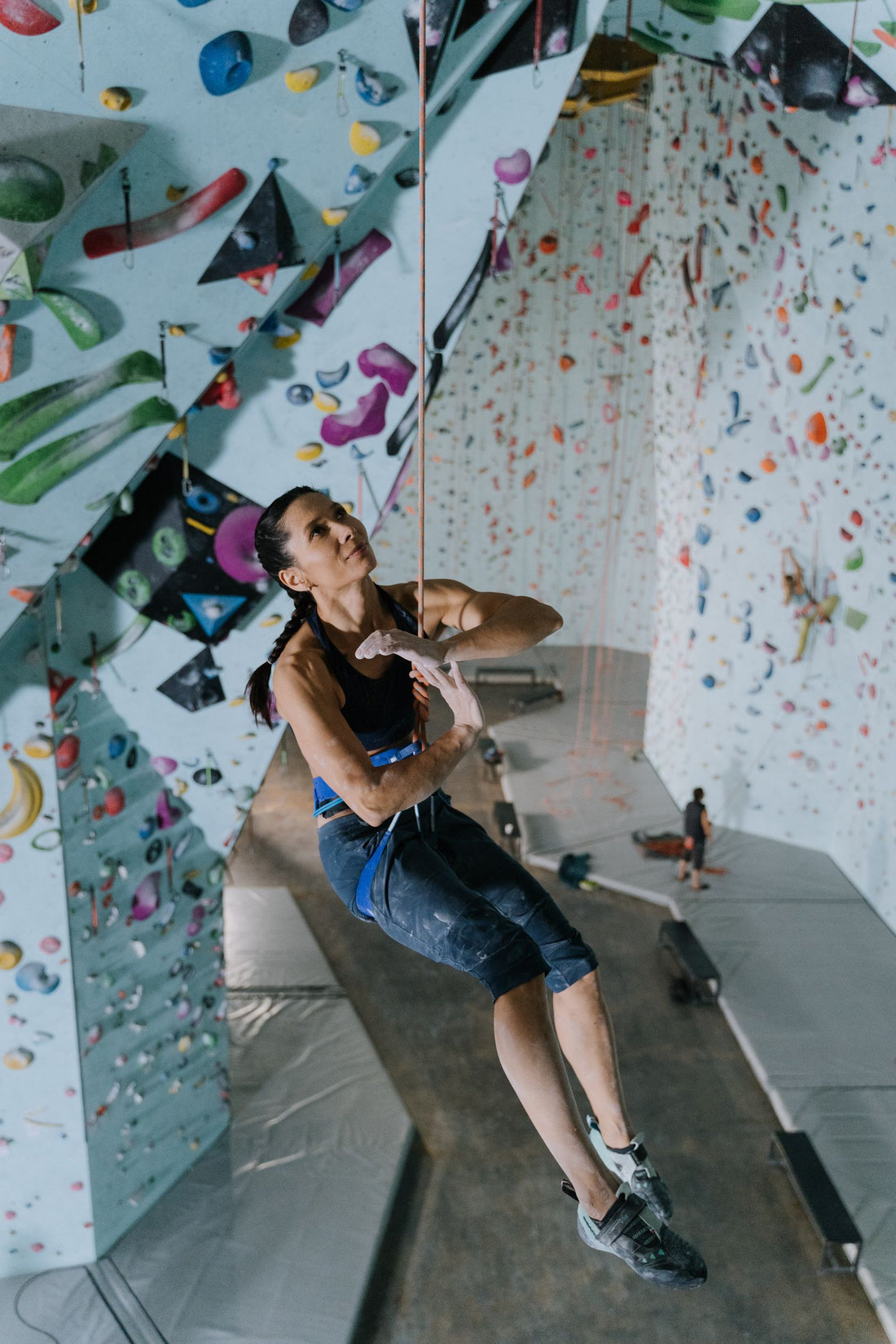 A climber on an indoor wall with the rope running down to her harness
