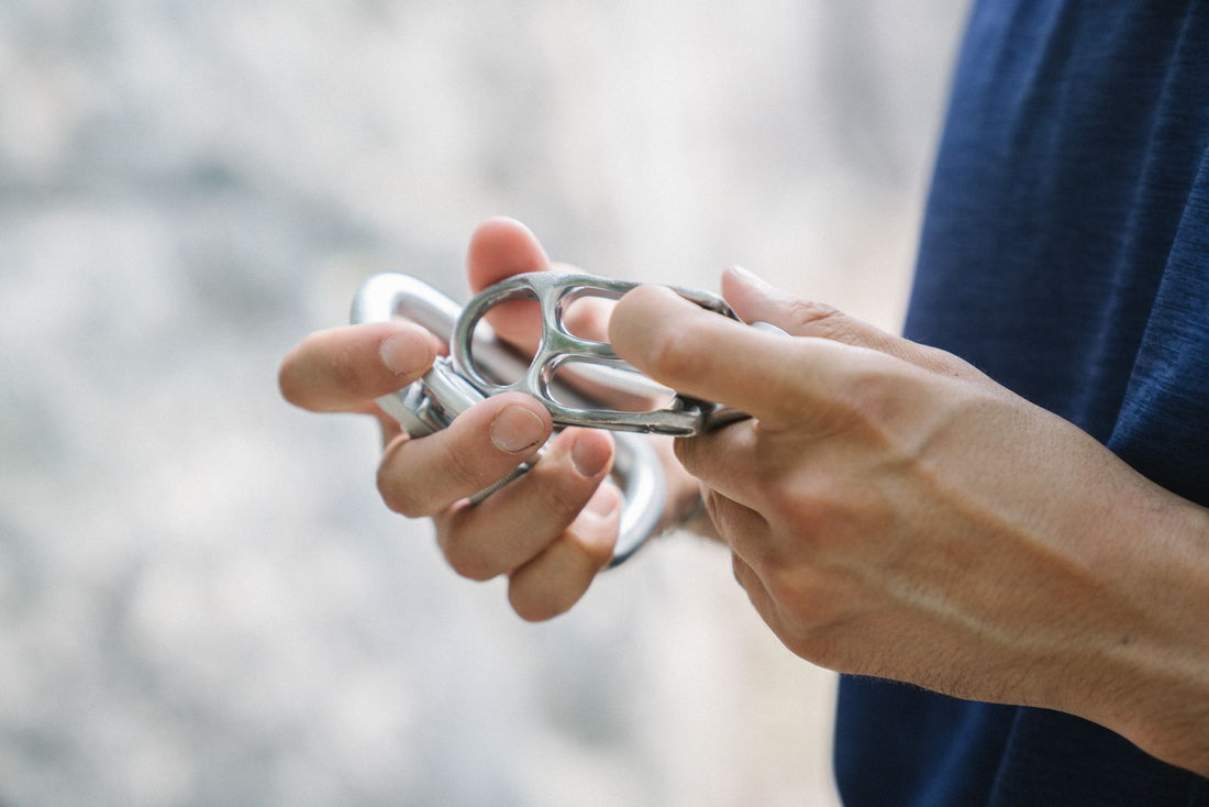 Hands holding a shiny silver climbing carabiner