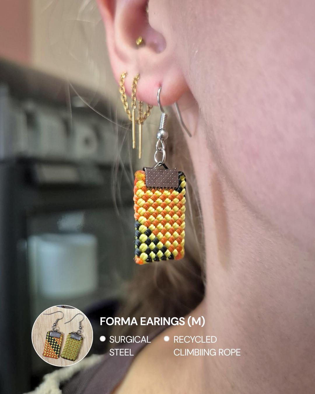 A pair of earrings cut from recycled climbing rope, held in a hand